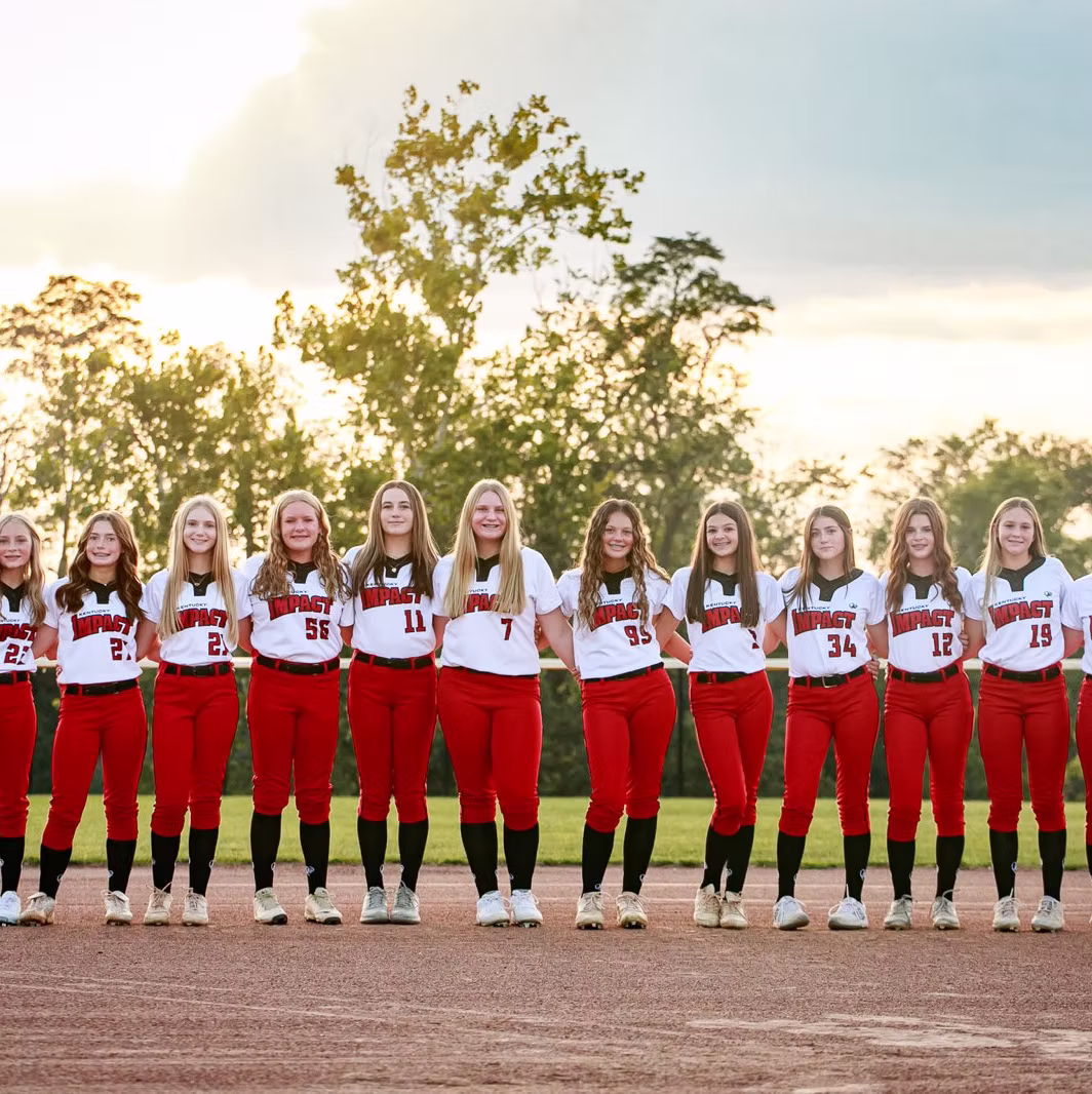 Softball team posing on field at sunset.