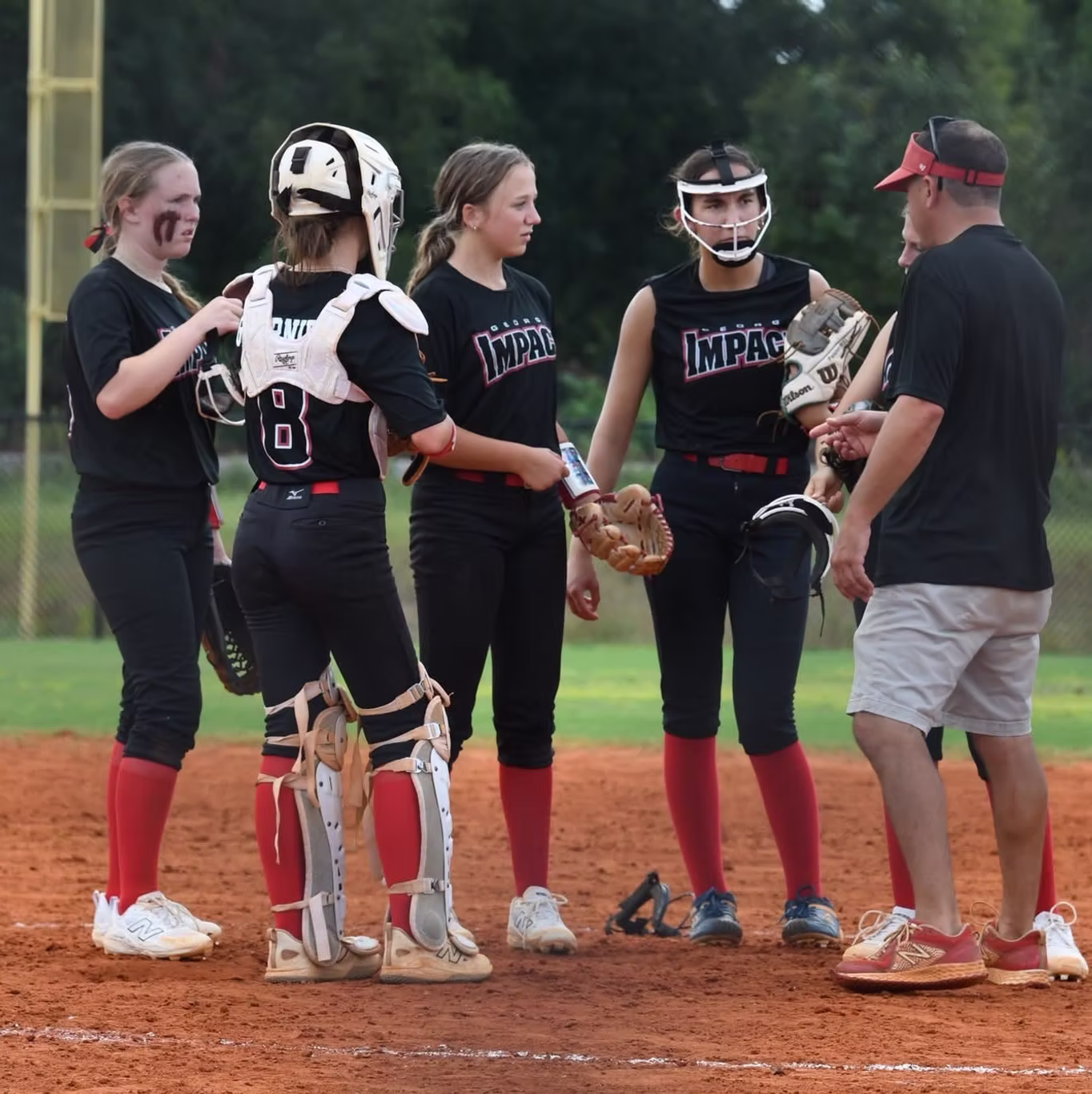 Softball players and coach discussing on field.