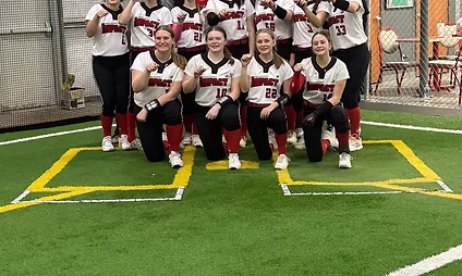 Softball team posing indoors on turf field.