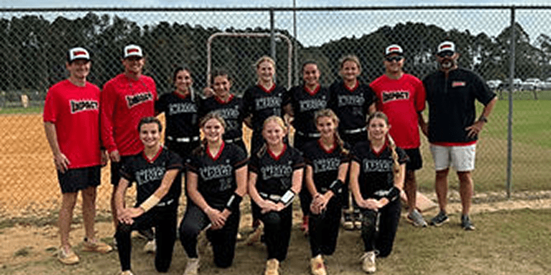 Softball team posing on field, smiling together.