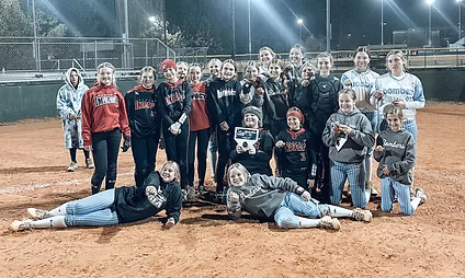 Youth softball team posing at night with plaque