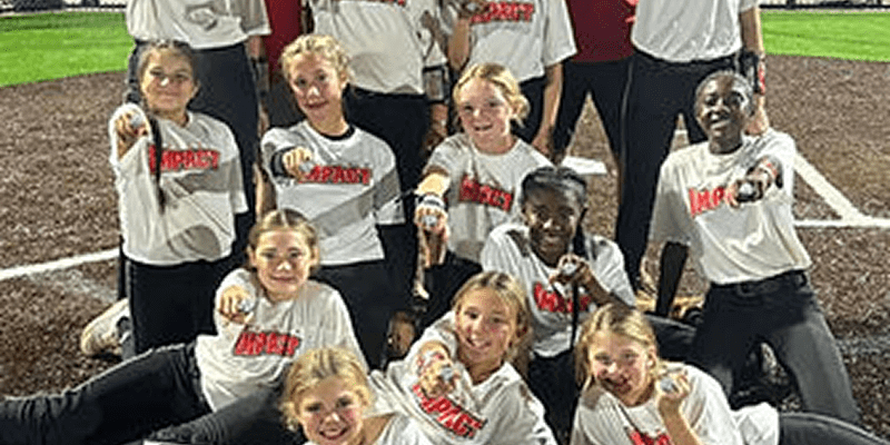 Smiling girls' softball team pointing on field