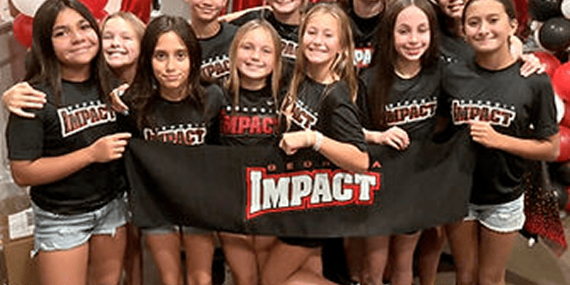 Group of girls holding "Impact" banner.