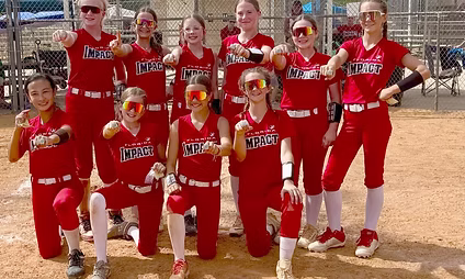 Softball team posing with medals on field.