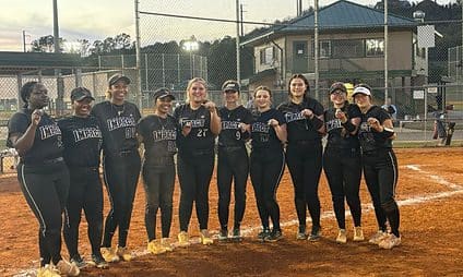 Softball team posing on dirt field together.