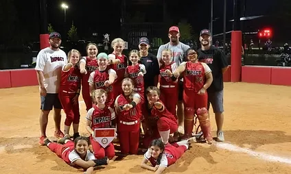 Softball team celebrating on the field at night.