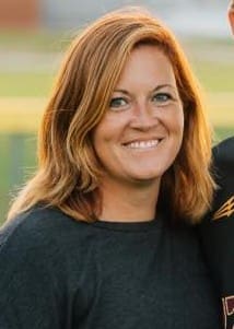 Smiling woman with shoulder-length auburn hair outdoors.