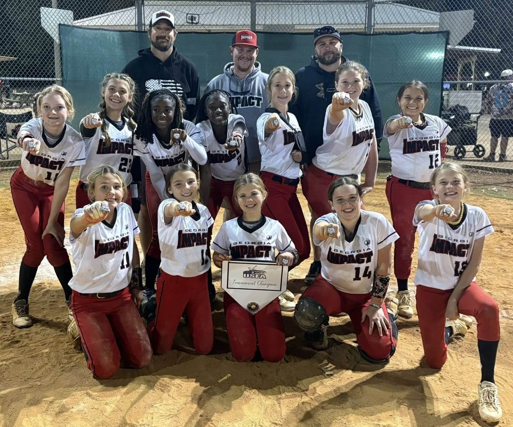 A softball team posing together on the field after a game.