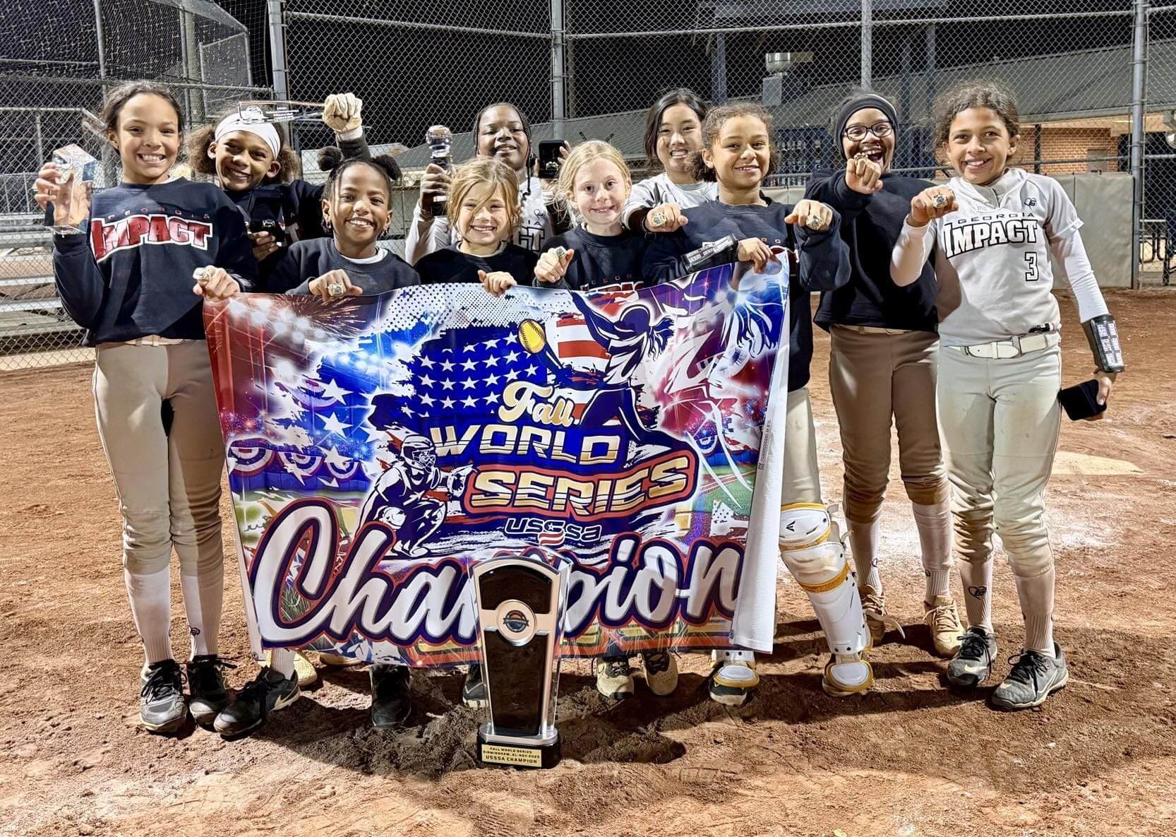 Softball team proudly holds World Series Champion banner and trophy.
