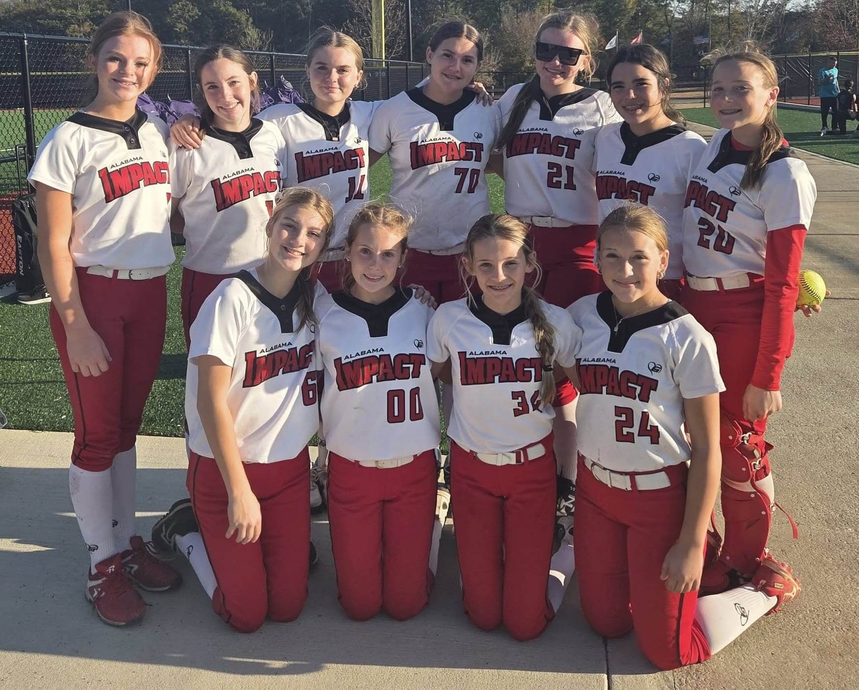 Softball team posing outdoors in matching uniforms on a sunny day.
