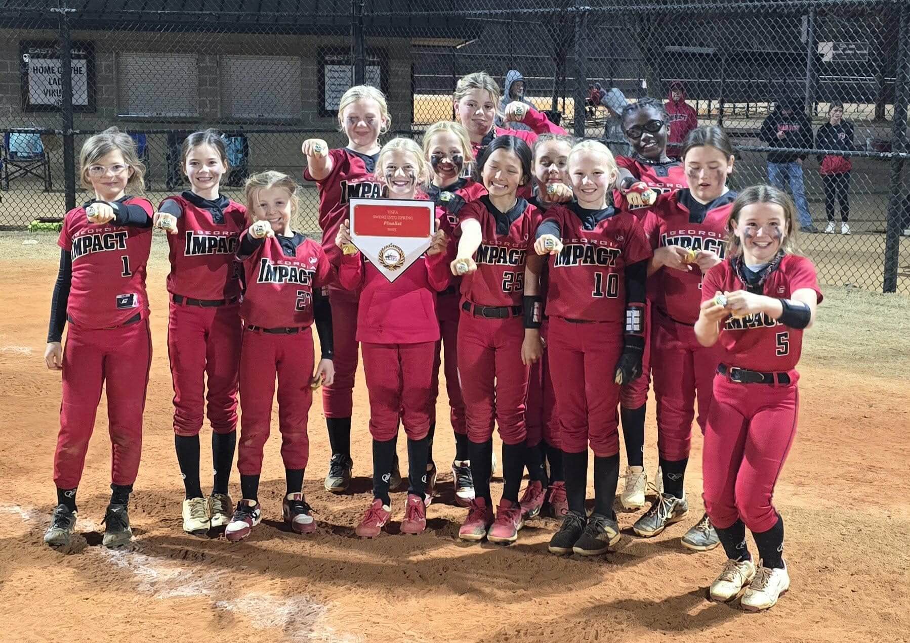 A softball team in red uniforms posing happily with a trophy.