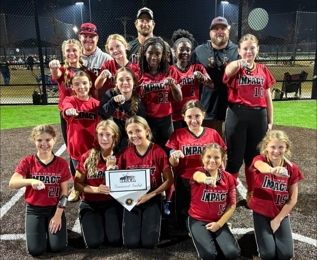 A softball team poses together in red uniforms holding a certificate.