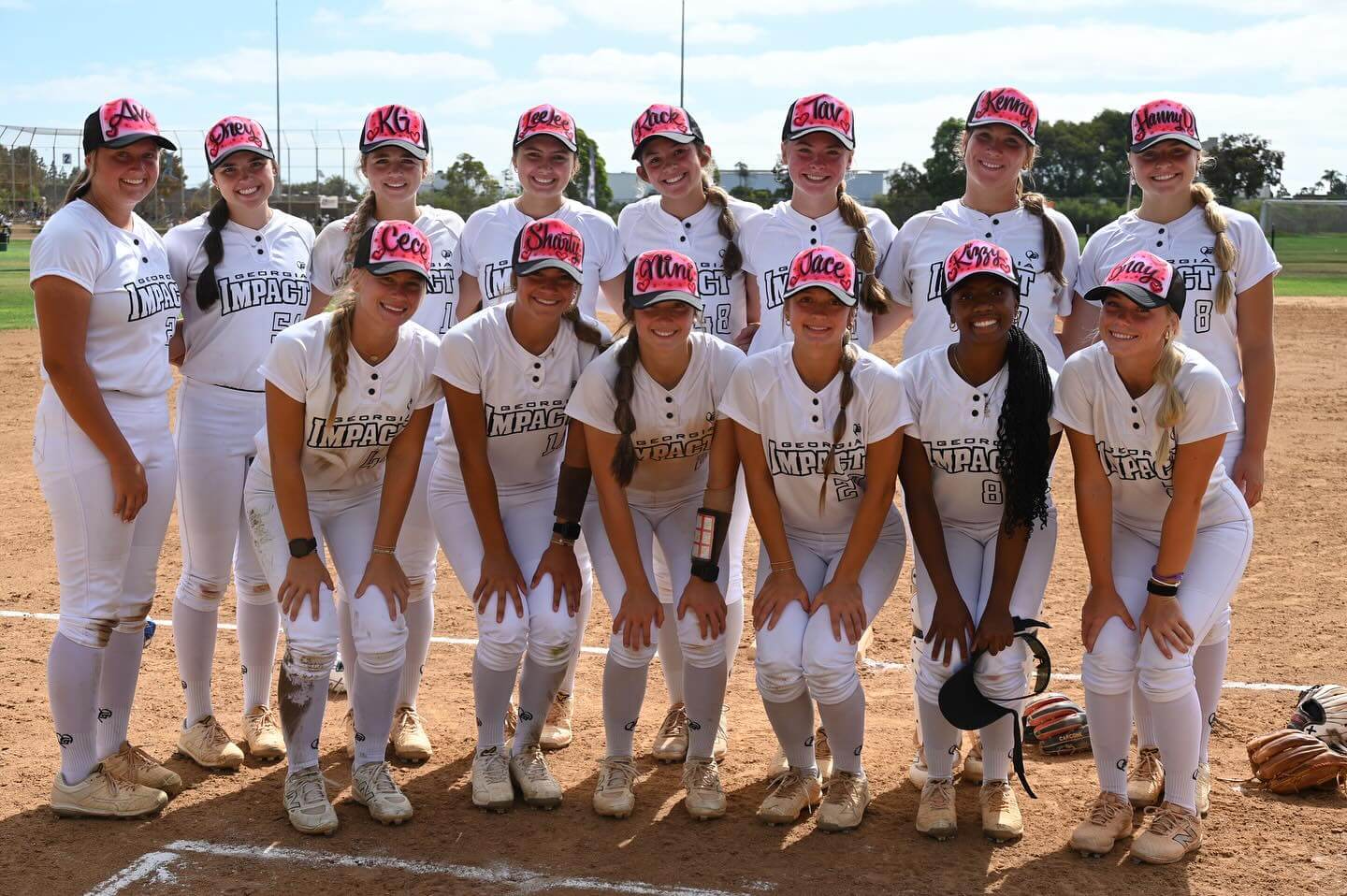A softball team posing on the field in white uniforms and red caps.