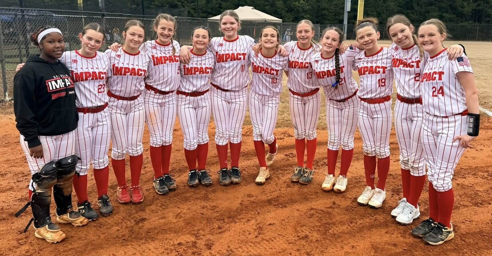 A girls' softball team posing together on a field in matching uniforms.