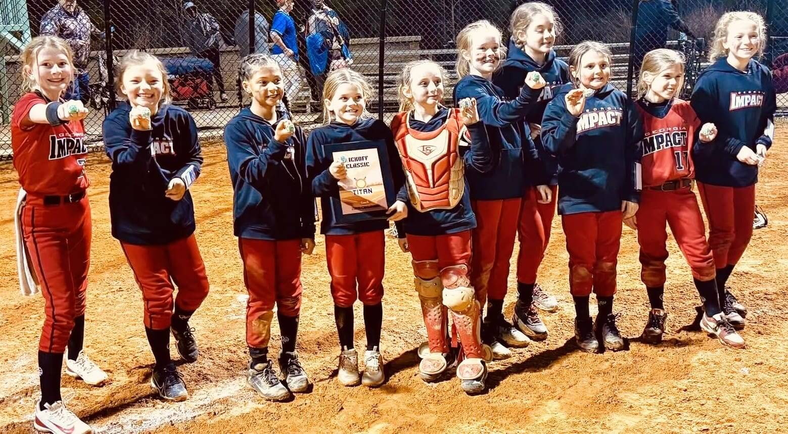Young softball players celebrating with a trophy on a field.